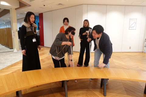 写真：アイマスクを付け、白杖を持ちながらオブジェに触る千葉と、それを横でサポートするリードユーザー